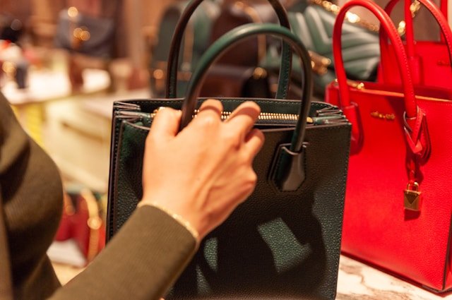 A hand holding onto a handbag, with other handbags around