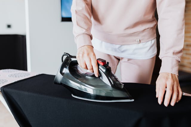 A person ironing clothes with an iron on an ironing board