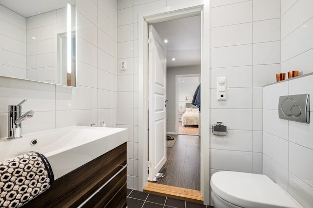 Photo of a small bathroom, showing a toilet, a sink, and a hallway beyond it